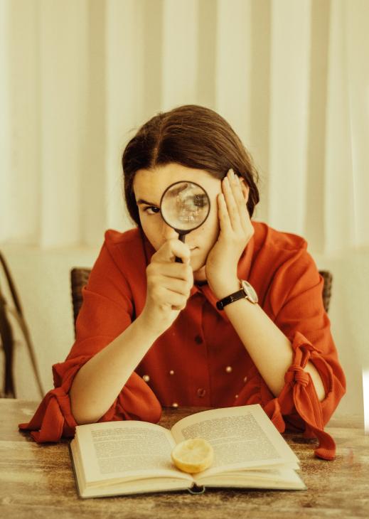 Jeune femme tenant une loupe devant son oeil